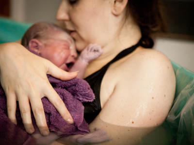 Image depicts a mum in a birthing pool, cuddling a newborn baby after giving birth