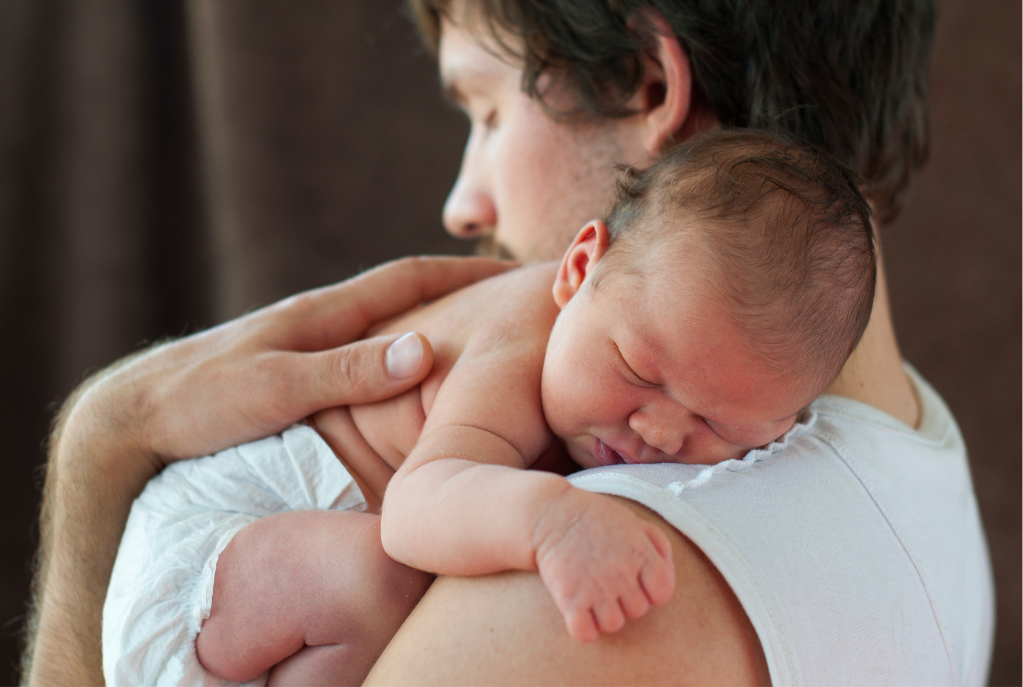 a father cradling a new born baby to his shoulder